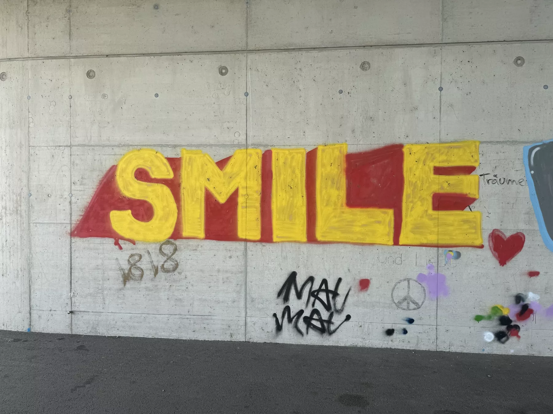 Gelbes SMILE-Graffiti mit rotem Schatten auf einer Betonwand an der Donau